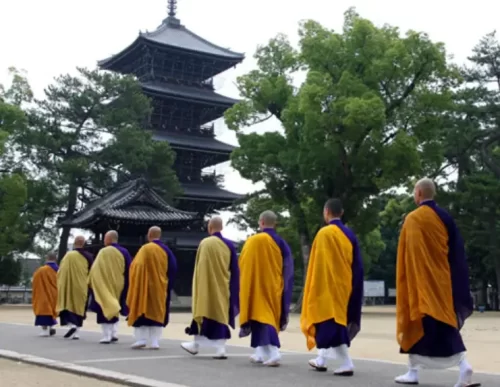 "A group of Buddhist monks walking in a line through the grounds of a Japanese temple, dressed in traditional robes, reflecting a peaceful and meditative atmosphere."