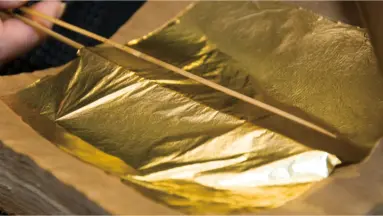 A craftsman delicately handling a thin sheet of gold leaf in Kanazawa, Japan — the city famous for its traditional gold leaf art.