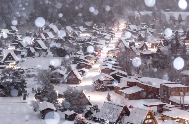 Snow-covered thatched-roof farmhouses of Shirakawa-go glowing with warm lights during a peaceful winter evening