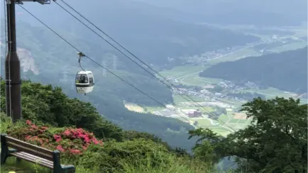 A scenic mountain view with a cable car ascending above a green valley and farmlands below.