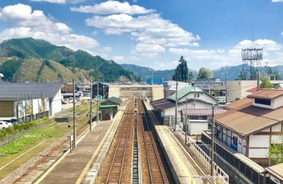 Takayama Station surrounded by mountain scenery under a bright blue sky in Gifu Prefecture, Japan.