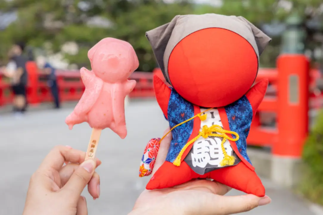 Sarubobo doll and strawberry ice treat held by travelers near Nakabashi Bridge in Takayama