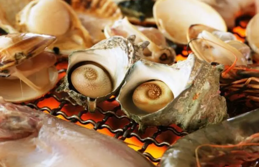 Fresh shellfish and turban shells grilling over charcoal at a Noto seafood restaurant