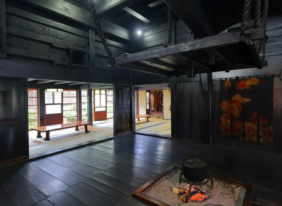 The interior of a traditional gassho-zukuri house in the Shirakawa-go Folk Museum, featuring an irori hearth, wooden beams, and tatami rooms.