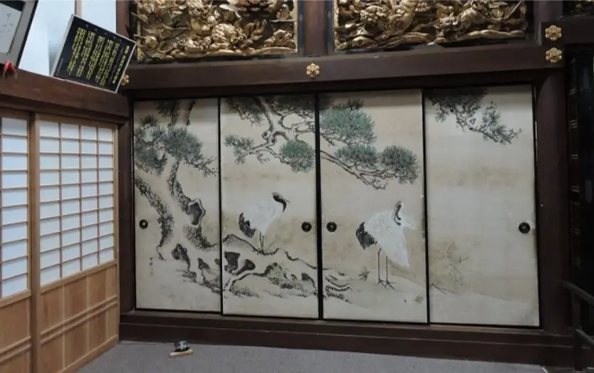 Elegant fusuma sliding doors decorated with traditional crane and pine tree paintings inside Myōzenji Temple in Shirakawago, framed by carved wooden beams.