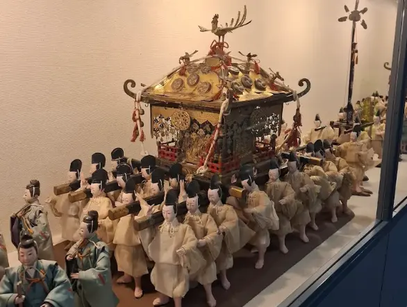 Miniature parade display of the Takayama Festival, featuring detailed figures carrying a decorated mikoshi inside the exhibition hall.