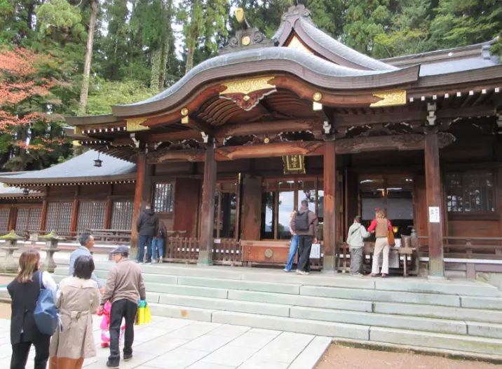 Visitors standing in front of the main worship hall of Sakurayama Hachimangu Shrine in Takayama, featuring traditional wooden architecture.