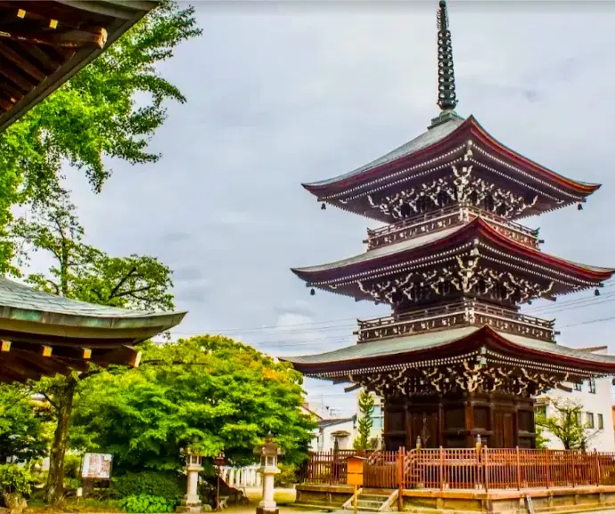 Three-story pagoda of Hida Kokubunji Temple in Takayama, featuring intricate wooden architecture surrounded by greenery.