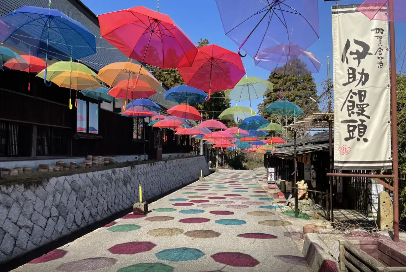 Colorful Japanese umbrellas suspended above a stone-paved walkway at Yunokuni no Mori, creating a vibrant and traditional atmosphere.