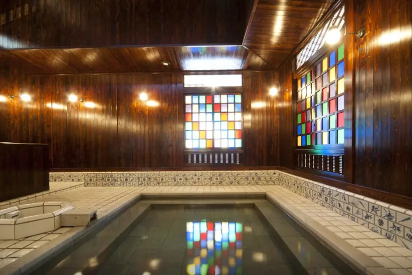 Indoor Japanese hot spring bath with stained glass windows and wooden interior