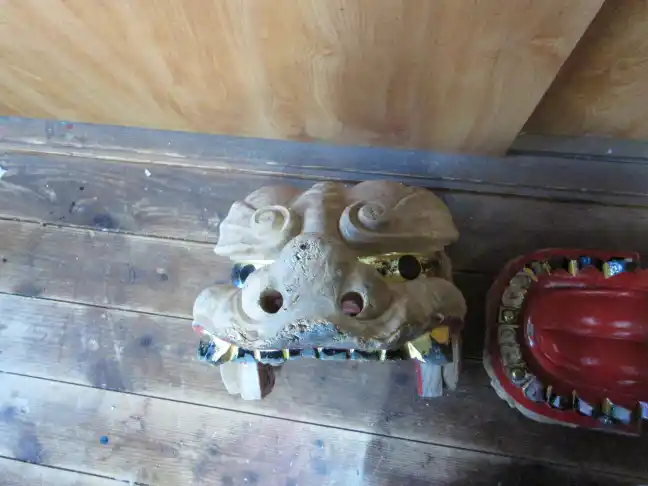 Disassembled traditional Shishi lion dance mask with wooden and lacquered parts resting on the floor of an artisan workshop before repair