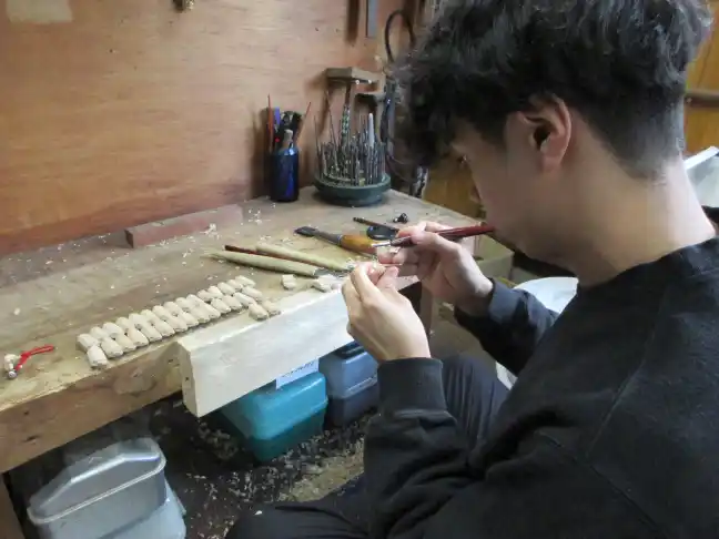 Skilled Japanese wood carving artisan shaping small wooden components for a festival Shishi lion mask in a traditional workshop