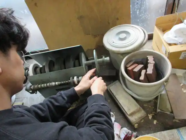 Skilled artisan carefully sharpening wood carving chisels using a grinding wheel in a rustic Japanese workshop