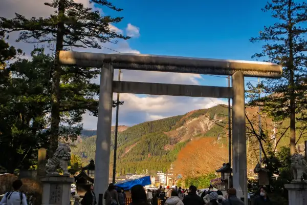 Large stone torii gate at the entrance of a shrine in the Hakusan area, with mountains in the background and visitors walking through.