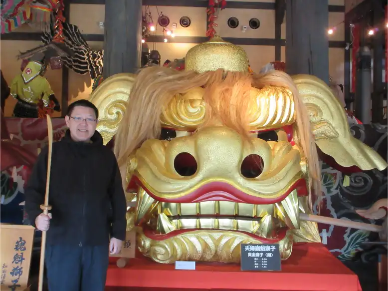 Traveler posing beside an enormous golden Shishi lion festival float head at a historic Japanese shrine cultural site
