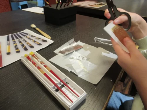 Participant cutting and applying gold leaf by hand during a traditional craft experience in Kanazawa