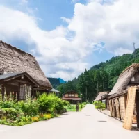 Bright summer scene of Gokayama with thatched gassho-zukuri houses lining a quiet village street surrounded by lush green mountains.